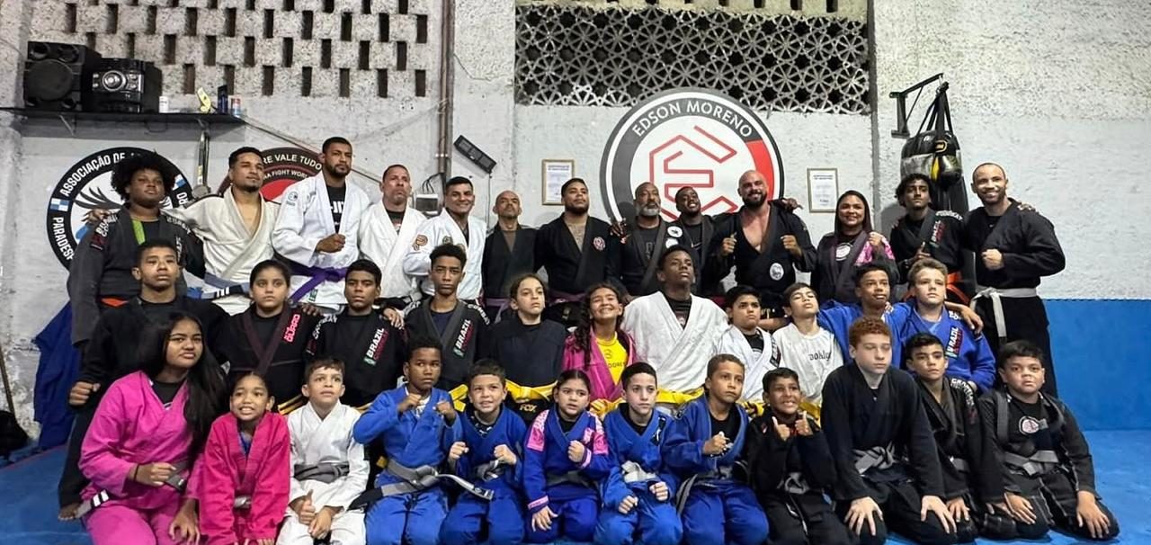 Turma do polo reunida no tatame: crianças, jovens e professores de quimono, com faixas de várias cores.